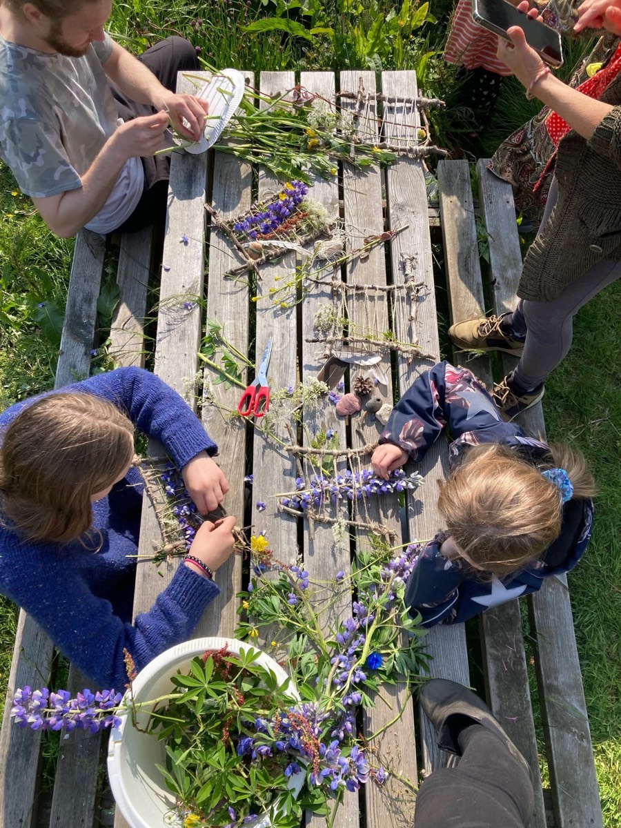 Children and adults weaving with sticks and wildflowers at a garden table